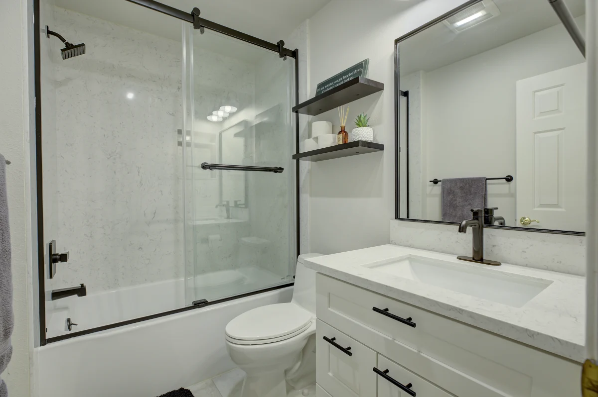 Bathroom with a sliding glass tub door, white vanity and black fixtures