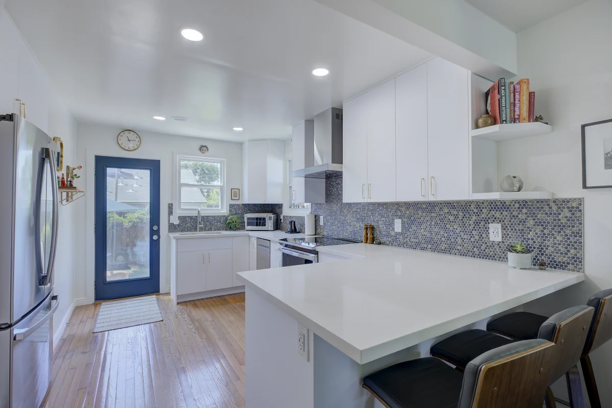 White kitchen with a peninsula, black stools and a blue door