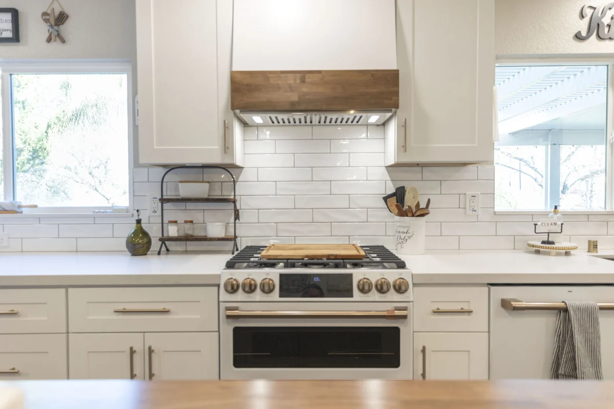 White kitchen with a wood range hood and subway tile