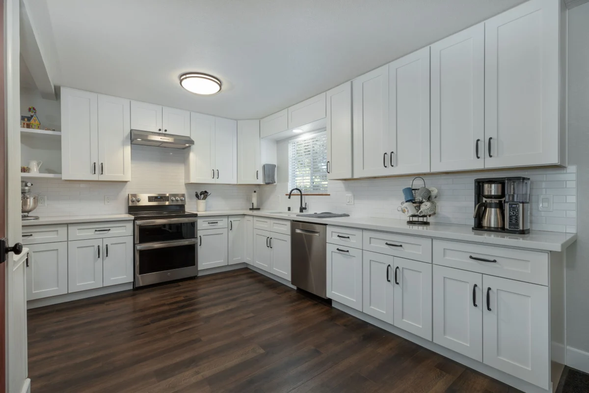 White L-shaped kitchen with dark wood-look floors