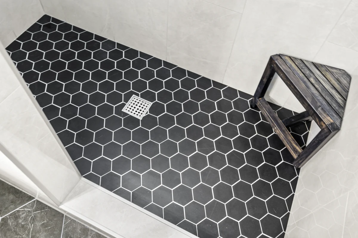 Shower floor with black hexagon tile and a teak stool