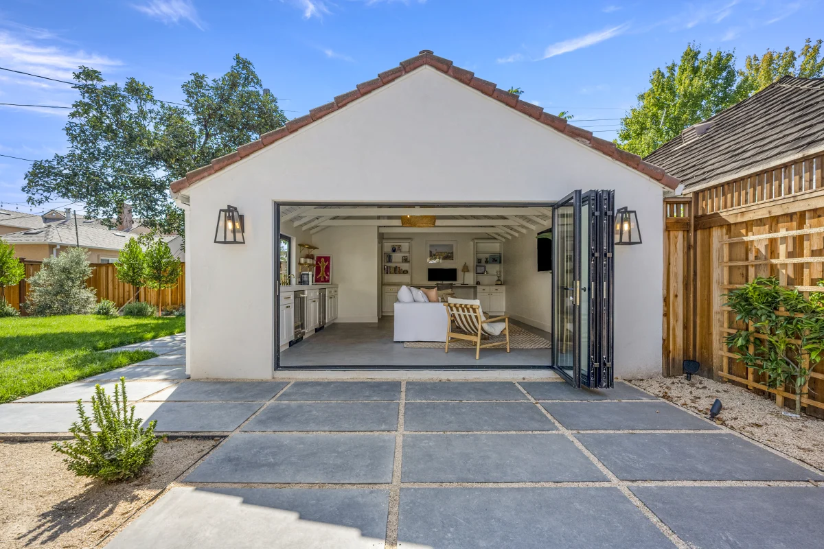 Converted garage with folding glass doors open onto a paved patio