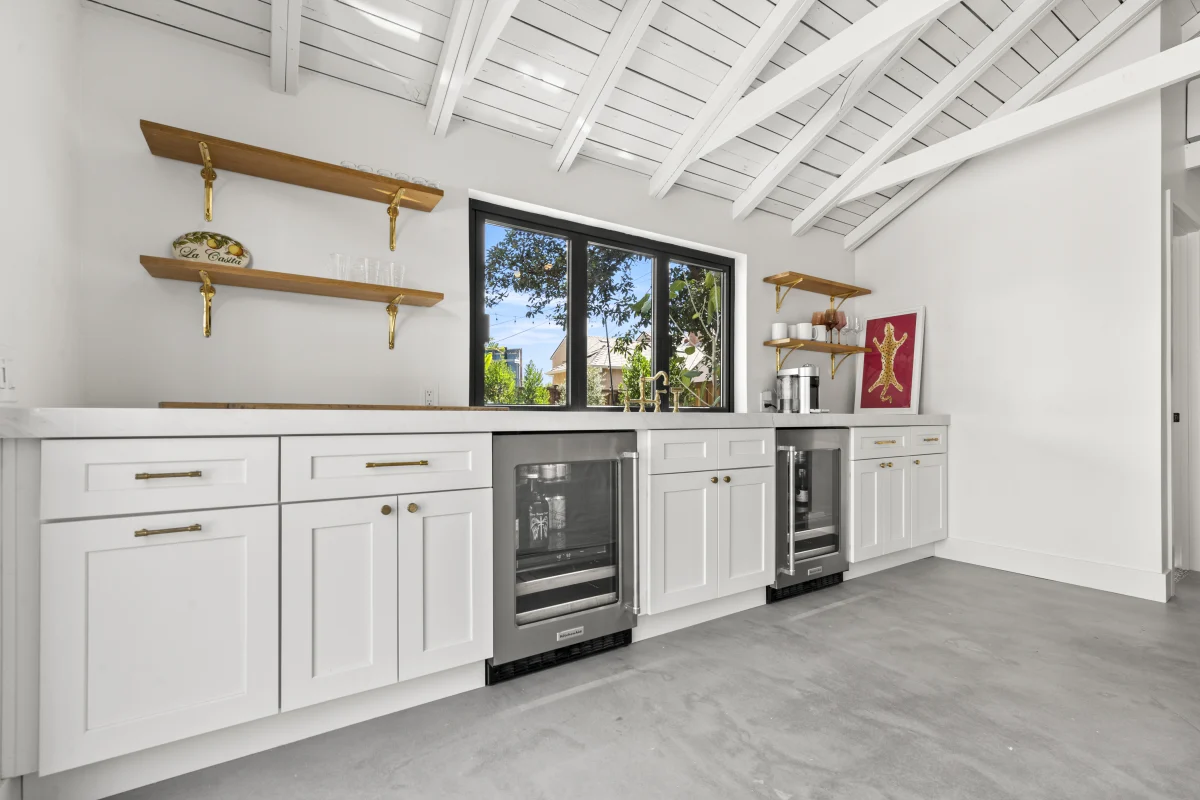 Converted garage with white cabinets, a wine fridge and open wood shelves