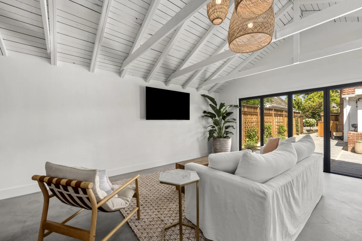 Converted garage lounge with a white sofa, a wall TV and glass doors to the yard