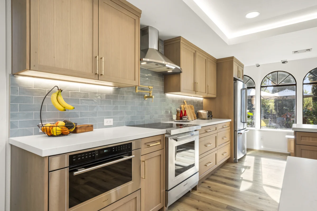 Kitchen with light wood cabinets, a blue tile backsplash and stainless appliances