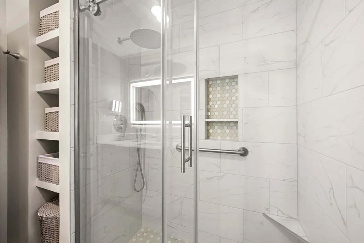 Glass shower with marble-look tile and a lit mirror