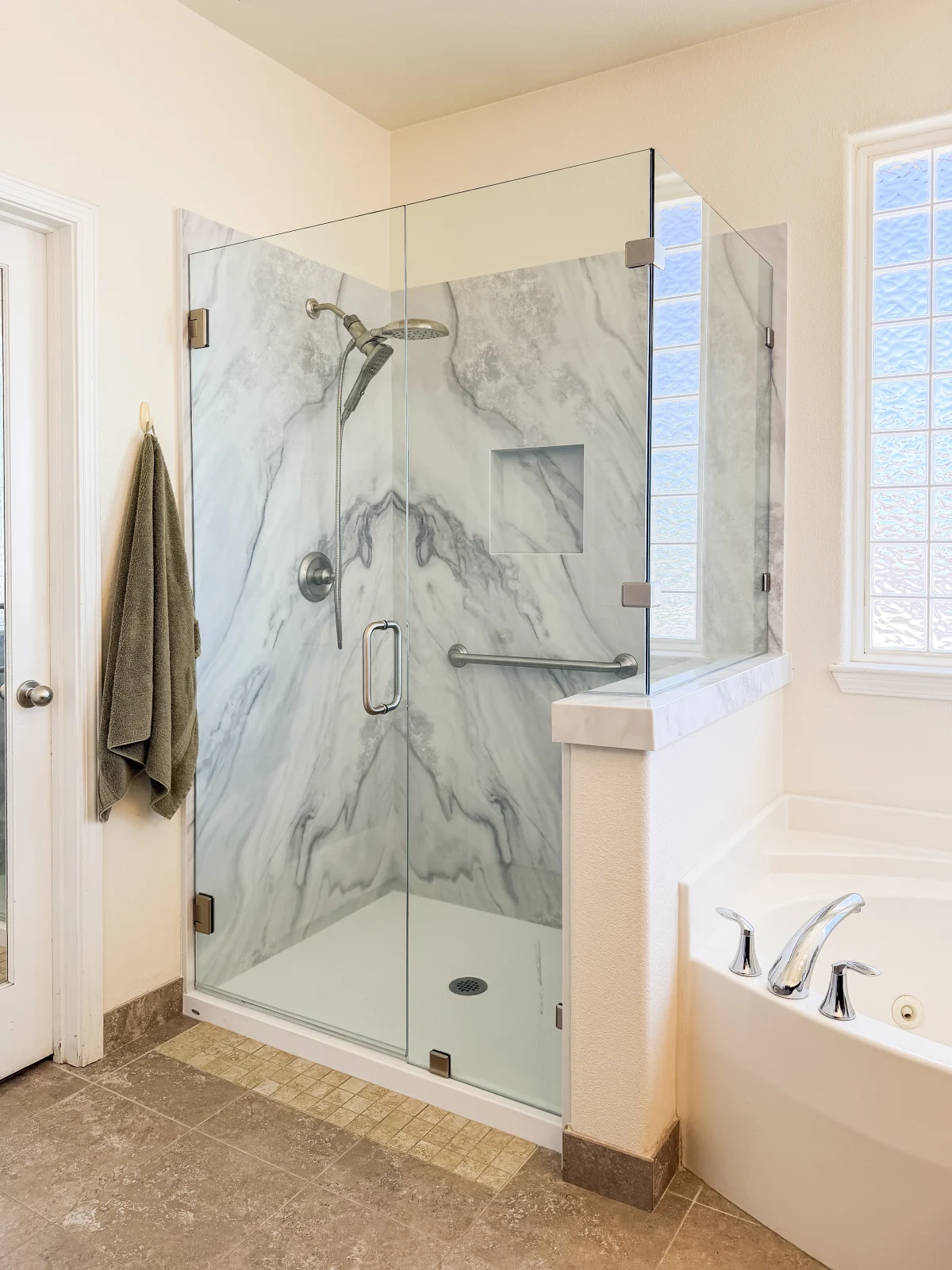Glass shower with marble-look walls beside a tub