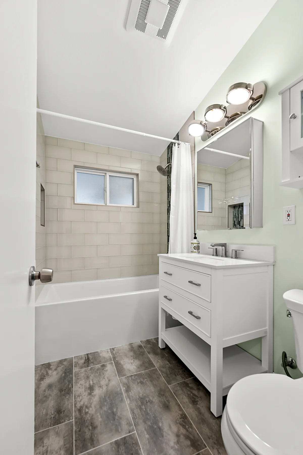 Bathroom with a white vanity, tiled tub surround and wood-look floor