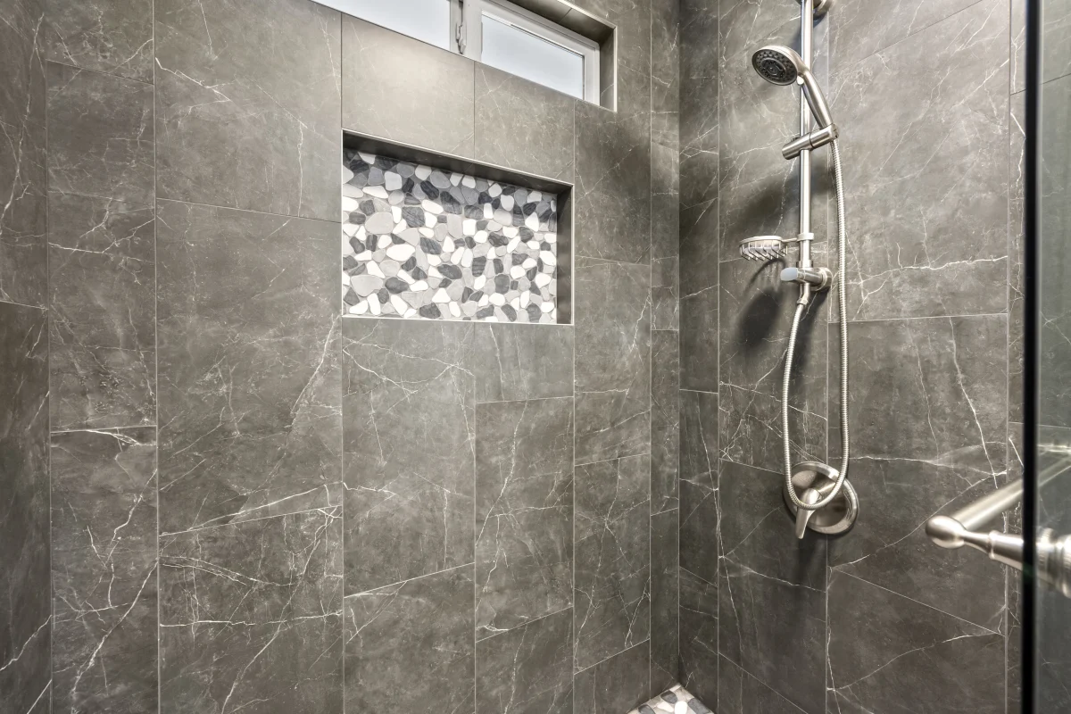Shower with dark gray tile and a mosaic niche