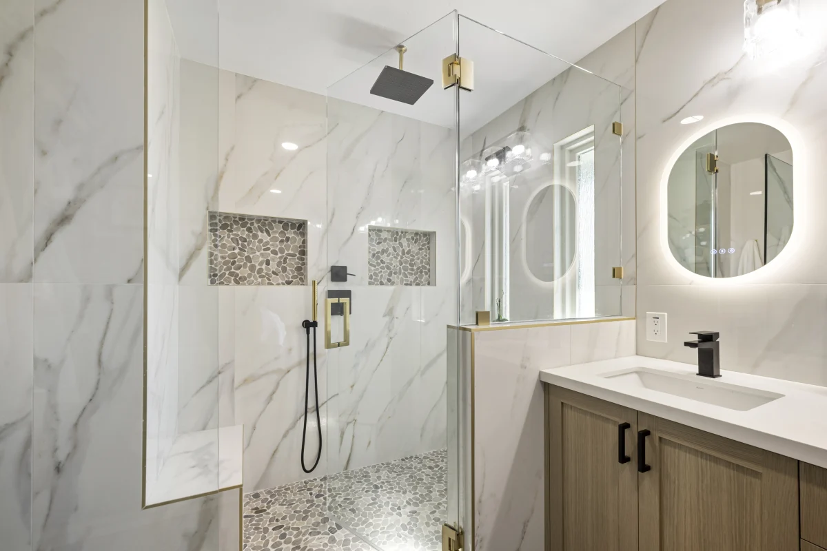 Walk-in shower with marble-look tile and a round lit mirror