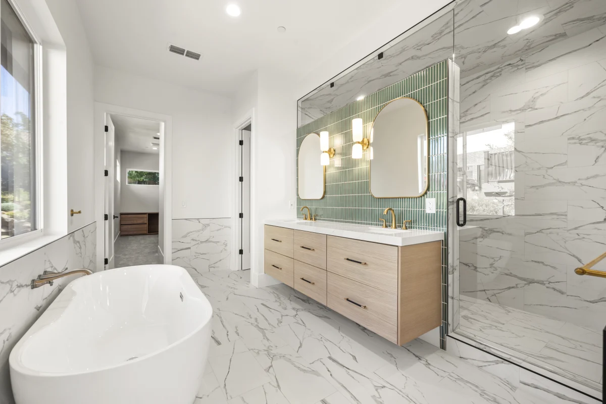 Remodeled bathroom with a green tile accent wall, brass fixtures and a freestanding tub, in a custom home by Solid Construction & Design