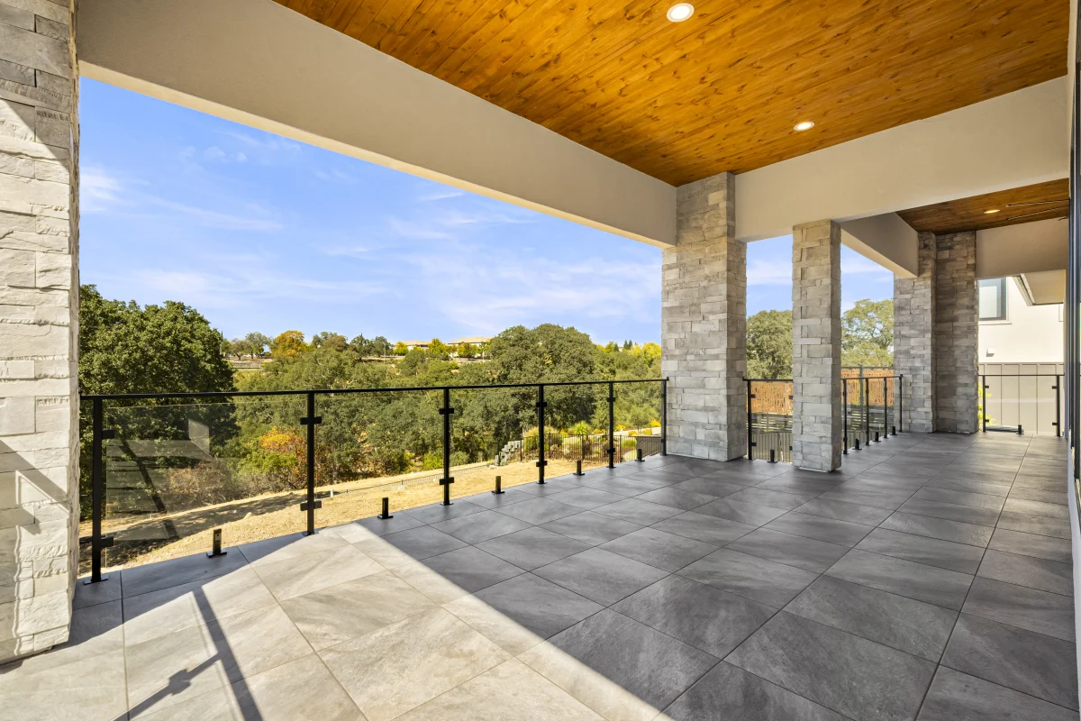 Covered upper terrace with a cedar ceiling, stone columns and a glass rail, looking out over the trees