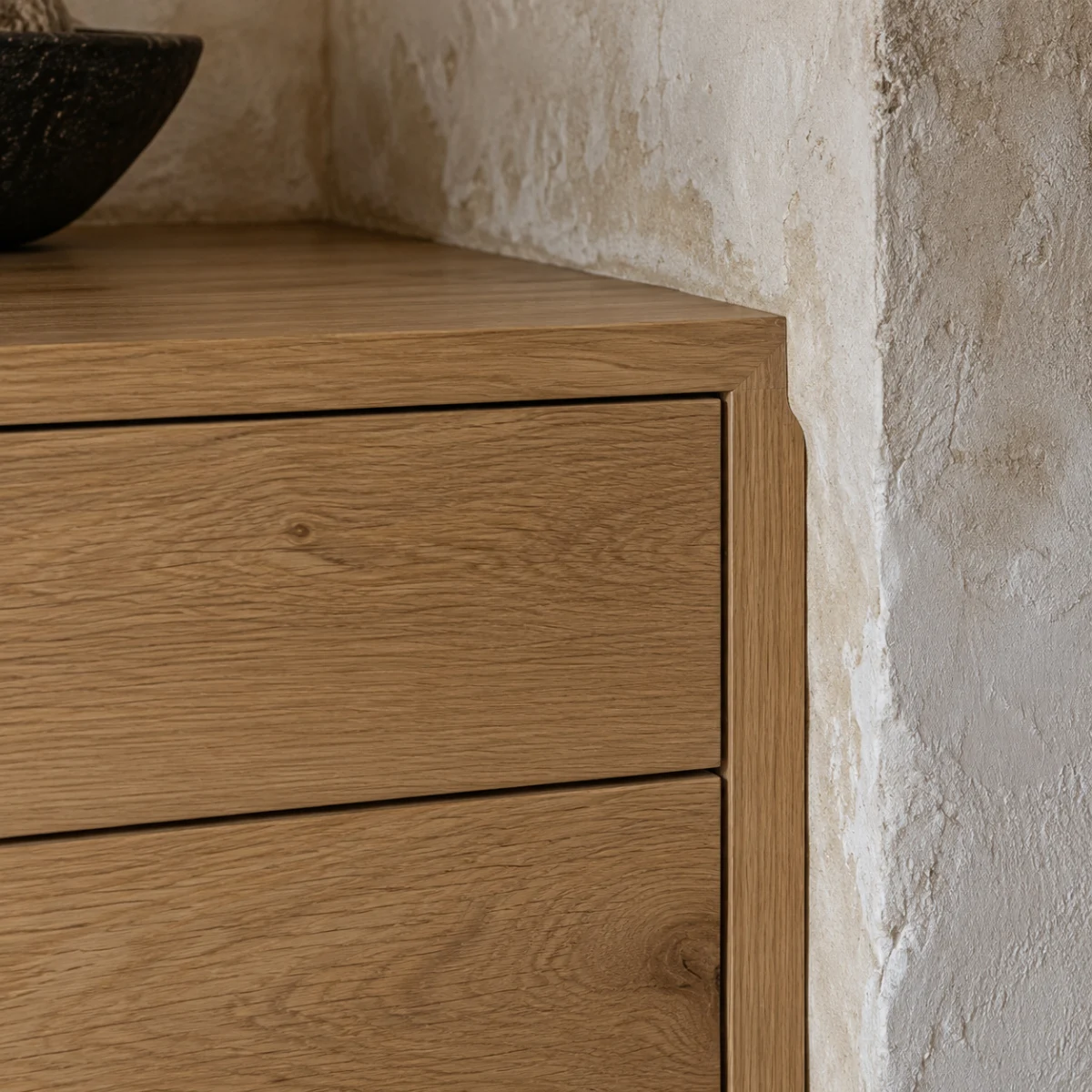 Close-up of a white oak cabinet corner against a plaster wall