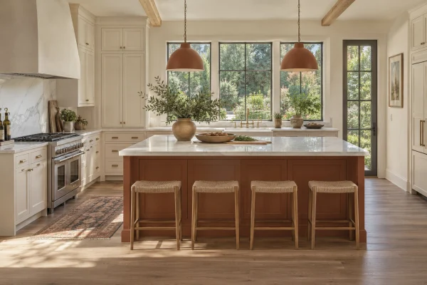Kitchen with a terracotta island, white cabinets and copper pendants