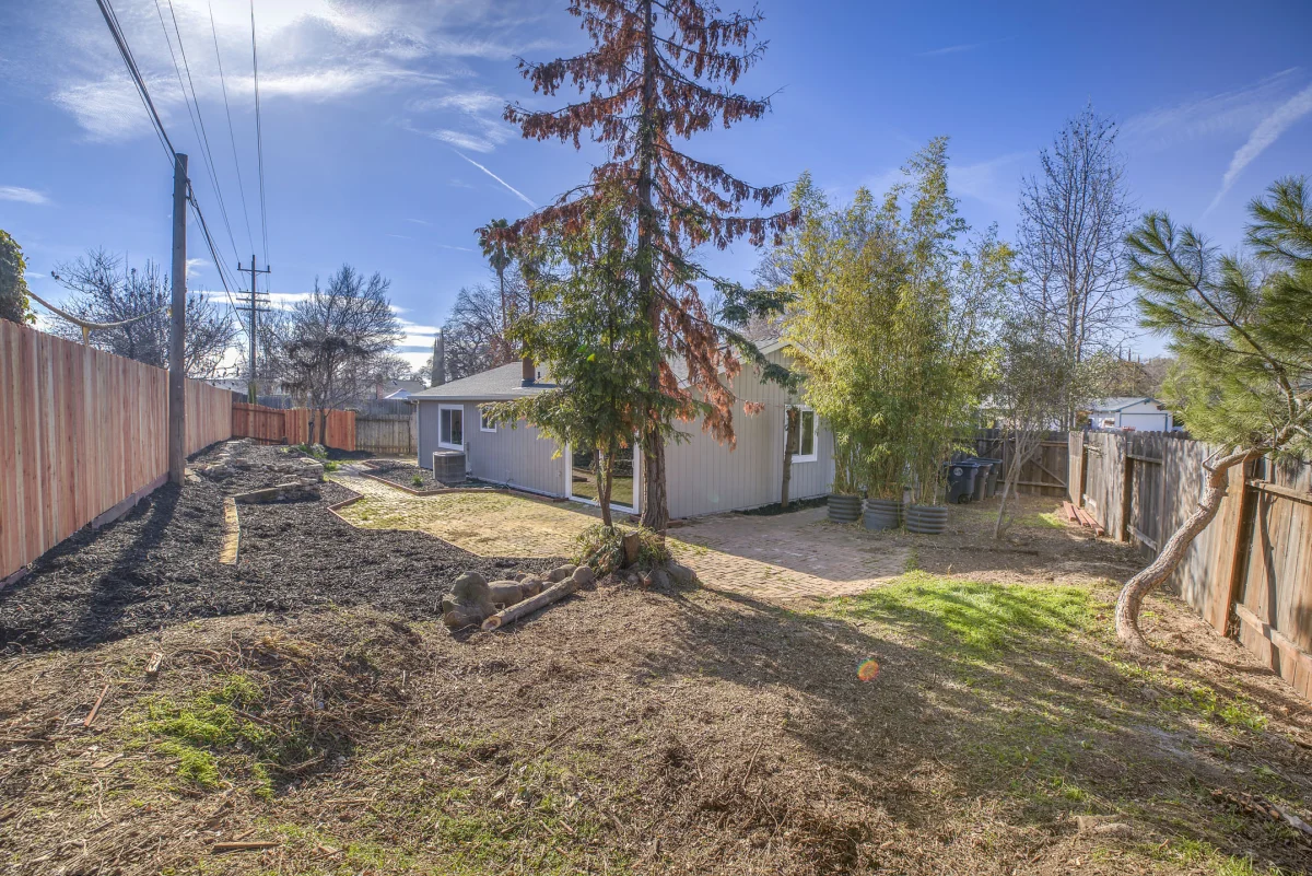 Fenced backyard with bare soil and trees behind a single-story house